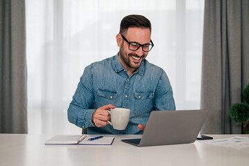 Smiling professional having coffee while working on laptop at office