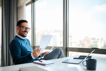 Smiling business professional reading documents while sitting at office desk