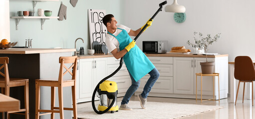 Young man having fun while vacuuming carpet in kitchen