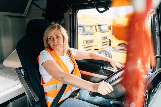 Mature Woman Truck Driver Steering Wheel Inside Lorry Cabin. Happy Middle Age Female Trucker Portrait 