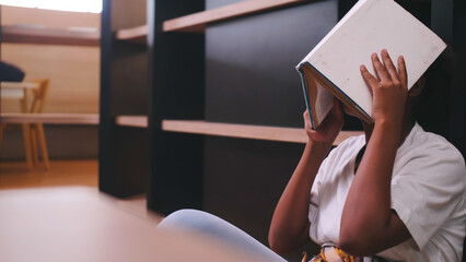 A schoolgirl is bored with reading books while preparing for exams while sitting in the library.