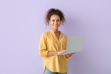 Pretty African-American woman using laptop on lilac background