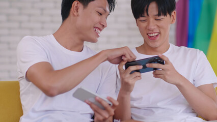 Happy gay Asian couple spending time together in living room at home.
