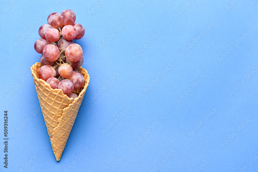 Wall mural Wafer cone with tasty grapes on blue background