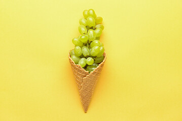 Wafer cone with fresh green grapes on color background