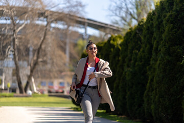 Happy young woman in white pants and a white shirt walking in the summer park