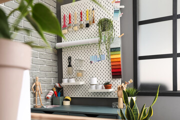 Pegboard with decorator's tools and houseplants in stylish workshop