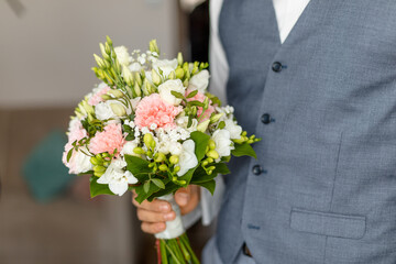 Hand of groom in wedding suit holding soft bridal bouquet of fresh flowers closeup. Elegant attribute of bride image and wonderful tradition. Beautiful and romantic wedding, luxurious celebration