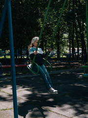 Obraz premium Happy child on a swing in sping park on vacation. Cute little girl with long blond hair swinging on a playground alone in tree shadow. Joy, fun, summer activities on fresh air.