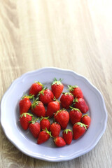 Lilac plate full of fresh strawberries on wooden table. Selective focus.