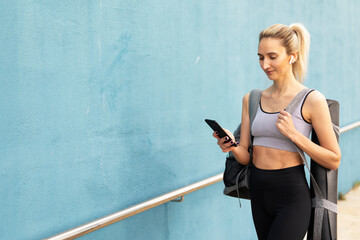 Young woman resting after running outside. Beautiful woman in sportswear using the phone.