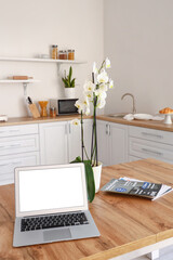 Modern laptop, orchid flower and magazines on dining table in kitchen