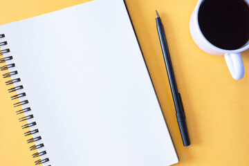 Directly above view of notepad, pen and coffee cup on yellow background.
