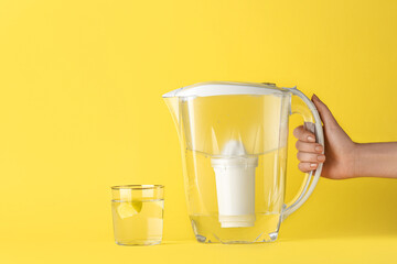 Woman with filter jug and glass of water with lemon slice on yellow background