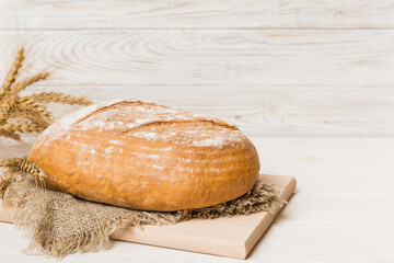 Freshly baked bread on cutting board against white wooden background. perspective view bread with copy space