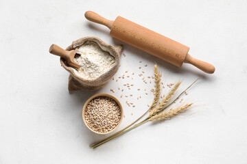 Bag with wheat flour and rolling pin on white background