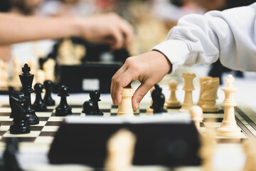 Chess on the street. Children playing summer vacation chess tournament. Child moving the rook in a chess game with the background out of focus and selective focus. Check the king. © Pixel_Studio_8