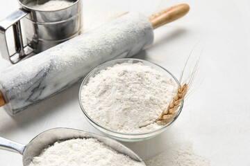 Bowl with wheat flour and rolling pin on white background, closeup