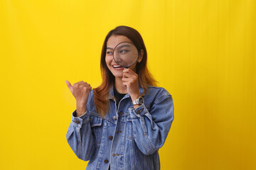 Young asian woman holding magnifying glass while presenting something sideways