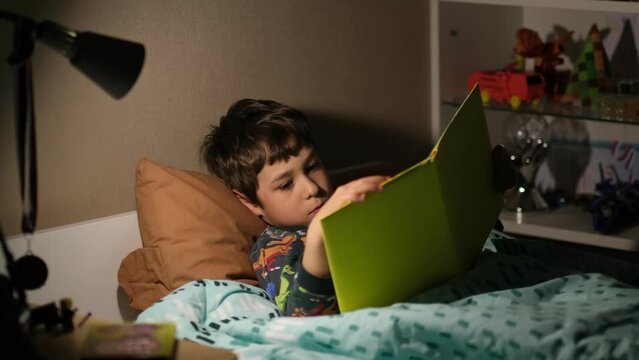 little boy reads a book on his own before going to bed.