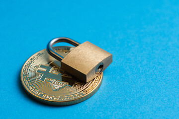 Tiny brass padlock on a shiny golden bitcoin on blue background.