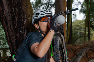 Close-up of a female cyclist sitting in the middle of a forest while hydrating and resting