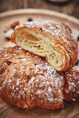Close up of delicious almond croissant bakery cut in half, served on wooden tray.