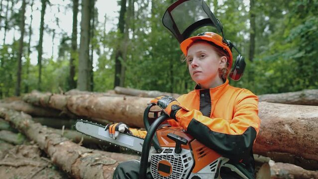 Portrait of a female logger sitting in the forest, young specialist in protective gear looks at the camera, hard work, 4k slow motion.