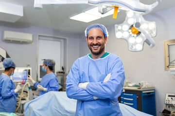 Portrait of male surgeon standing with arms crossed in operation theater at hospital. Team surgeons are performing an operation, middle aged doctor is looking at camera, in a modern operating room - obrazy, fototapety, plakaty