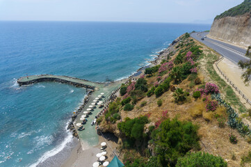 An overhead view of the pier into the sea, with the beach, rocks and road