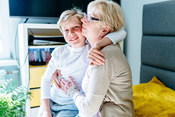 Handsome cute grandson huging his lovely grandmother in his room at home. Happy family relationships, love, caring for an old woman.