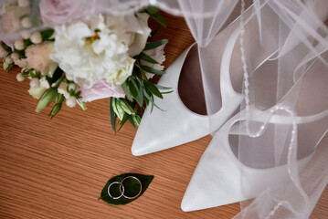 Bridal bouquet of roses and greenery with satin ribbon, women shoes and two golden wedding rings on...