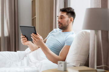 technology, internet and people concept - man with tablet pc computer in bed at home bedroom