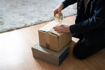 person's hands sealing big cardboard box with tape for shipment.