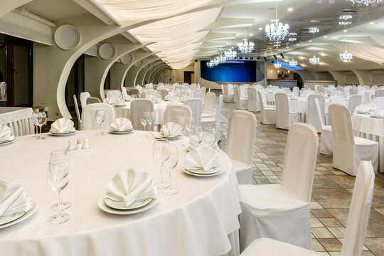 Banquet hall decorated in white with round served tables and stage for performance