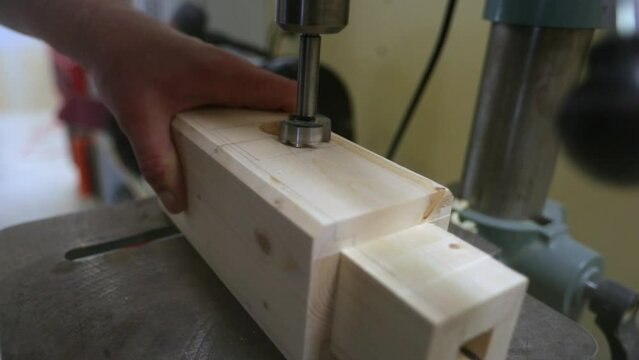 Drilling out a tenon slot in a wood beam on a drill press in slow motion as wood chips are displaced in every direction.