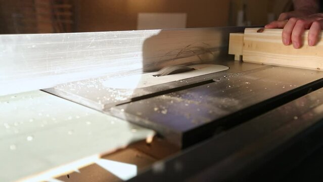 A woodworker rotates a piece of wood and pushes it over a table saw with multiple passes to make tenons from a piece of wood using a dado set in slow motion.