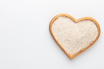 Wheat flour in a wooden heart shape bowl on a pastel background.