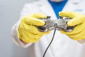 A doctor in a medical gown and protective gloves holds a gamepad in his hands. The face is not...