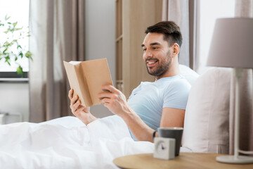 people and rest concept - man reading book in bed at home