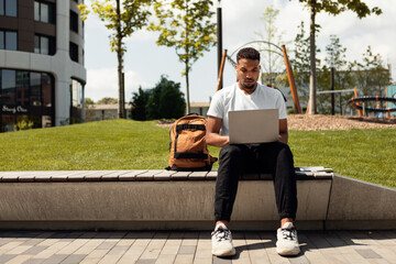 Rest in the city. African american male student relaxing outdoors with laptop, sitting in park,...