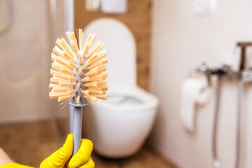 Toilet brush in hand in a yellow glove close-up. Bathroom and toilet background