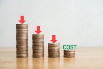 Arrow press push down on stacks coin for control cost reduction with white wall background on wooden table. Concept of cost reduction, cost cut in business or production, optimize improvement.