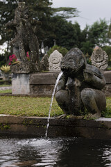 Fototapeta na wymiar Frightening sculpture of beast or demon of balinese mythology as fountain in majestic park Tirta Gangga on Bali, vertical. Old monument of balinese culture, religion and history.
