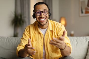 Smiling young African American man in headset chatting online, having webinar or video conference...