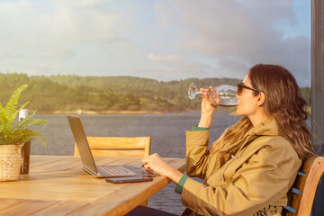 Entrepreneurial Latin woman enjoys the scenery while sitting in front of her computer and drinking from a crystal glass
