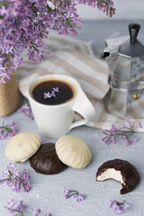 Cup of coffee, lilac, marshmallow in dark and white chocolate glaze, coffee maker. Still life