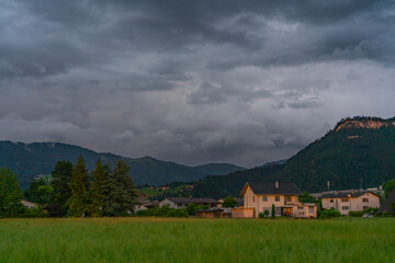 Fototapeta na wymiar House at dusk after sunset in Dornbirn, Vorarlberg, Austria. pink and grey-blue clouds over the green meadows, trees, barns and mountains. Interesting and impressive cloud mood