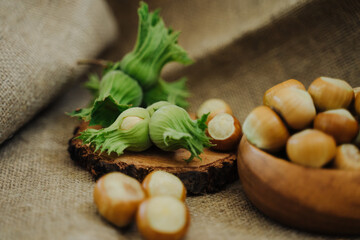Unpeeled hazelnuts in a husk next to a bowl with hazelnuts in leaves and peel. Hazelnuts or cobnuts with leaves. Healthy food concept. Fresh harvest of hazelnuts. 