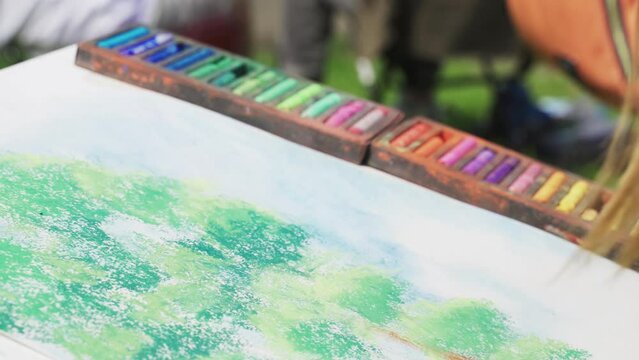 The girl draws a tree with green chalk on paper. Close-up of hands, multi-colored pastel crayons.